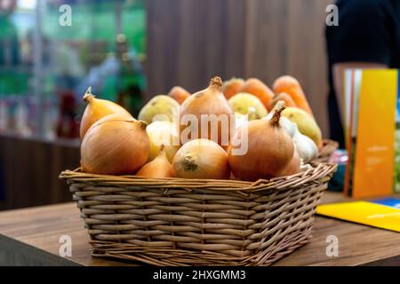 Zwiebeln, Knoblauch und Kartoffeln befinden sich in einem Weidenkorb Stockfoto