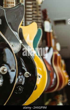 Reihe von E-Gitarren in einem Musikinstrumenteladen. Teile der Gitarre, Korpus, schwarz, blau, gelb, Blau Stockfoto