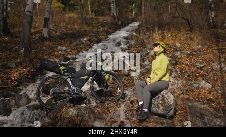 Die Frau reist auf gemischtem Terrain mit Bikepacking. Die Reise des Reisenden mit Fahrradtaschen. Sportswear in grün-schwarzen Farben. Die Reise i Stockfoto