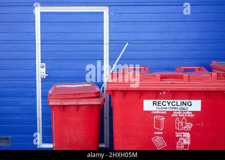 Zwei Mülltonnen, eine kleine und eine große, vor einem blauen Garagentor gesehen. Stockfoto