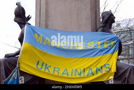 Manchester, Großbritannien, 12.. März 2022. Eine Flagge der „Manchester Ukrainer“ auf den Bronzefiguren auf der Statue des Herzogs von Wellington in Piccadilly Gardens, im Zentrum von Manchester, England, während eines Protestes über die russische Invasion in der Ukraine. Es wurde vom Ukrainischen Kulturzentrum „Dnipro“ Manchester organisiert. Die Medien haben berichtet, dass der russische Beschuss von Schulen, Krankenhäusern und Wohnungen in der Ukraine jetzt am 17.. Tag der Verteidigung des Landes durchgeführt wurde. Quelle: Terry Waller/Alamy Live News Stockfoto