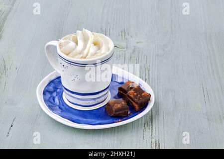 Tasse Kaffee mit Schlagsahne und gehackter Schokolade auf einem hellblauen Holztisch Stockfoto