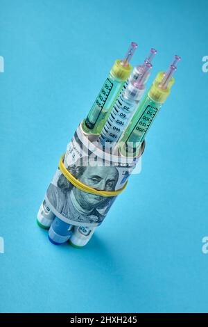 Insulin-Spritzenstifte in Dollarscheine auf blauem Hintergrund verpackt Stockfoto