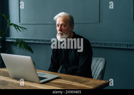 Müde ältere grauhaarige Mann Blick auf Laptop-Bildschirm fühlt sich verwirrt hat Schwierigkeiten mit dem Gerät, nicht verstehen, Hilfe beim Lernen benötigen. Stockfoto