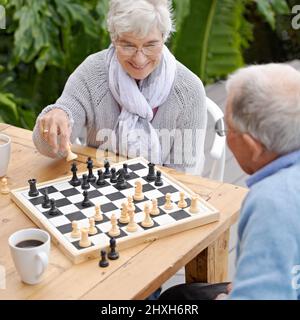 Diese nächsten Schritte werden mir das Spiel gewinnen. Ein älteres Paar spielt im Freien zusammen Schach. Stockfoto