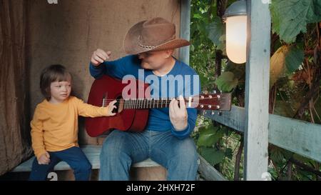 Papa Cowboy spielt für sein kleines Kind eine akustische Gitarre. Altes Retro-Dekor Stockfoto