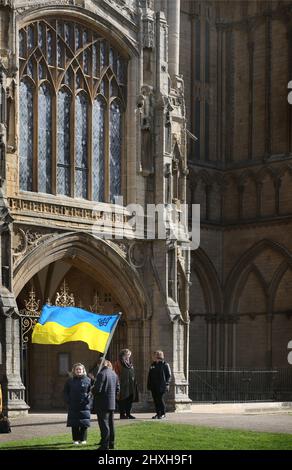 Peterborough, Großbritannien. 12. März 2022. Vor der Kathedrale wird eine ukrainische Flagge geschwungen. Zu einer Zeit, in der die Ukraine von Wladimir Putins Russland angegriffen wird, feiern die Litauer ihren Unabhängigkeitstag zur Wiederherstellung in der Peterborough-Kathedrale. Sie stehen zur Unterstützung der Ukraine und halten ukrainische Flaggen und Bänder fest. Am 11. 1990. März erlangte Litauen seine Freiheit aus der Sowjetunion zurück. Ein kurzes Gebet und eine Schweigeminute wurden für die gefallenen Verteidiger der Freiheit gehalten. (Foto von Martin Pope/SOPA Images/Sipa USA) Quelle: SIPA USA/Alamy Live News Stockfoto