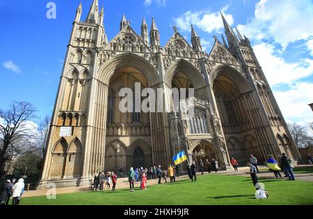 Peterborough, Großbritannien. 12. März 2022. Vor der Kathedrale wird eine ukrainische Flagge geschwungen. Zu einer Zeit, in der die Ukraine von Wladimir Putins Russland angegriffen wird, feiern die Litauer ihren Unabhängigkeitstag zur Wiederherstellung in der Peterborough-Kathedrale. Sie stehen zur Unterstützung der Ukraine und halten ukrainische Flaggen und Bänder fest. Am 11. 1990. März erlangte Litauen seine Freiheit aus der Sowjetunion zurück. Ein kurzes Gebet und eine Schweigeminute wurden für die gefallenen Verteidiger der Freiheit gehalten. Kredit: SOPA Images Limited/Alamy Live Nachrichten Stockfoto