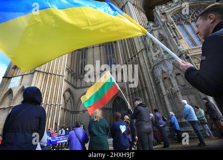 Peterborough, Großbritannien. 12. März 2022. Sowohl litauische als auch ukrainische Flaggen werden vor der Kathedrale geschwenkt. Zu einer Zeit, in der die Ukraine von Wladimir Putins Russland angegriffen wird, feiern die Litauer ihren Unabhängigkeitstag zur Wiederherstellung in der Peterborough-Kathedrale. Sie stehen zur Unterstützung der Ukraine und halten ukrainische Flaggen und Bänder fest. Am 11. 1990. März erlangte Litauen seine Freiheit aus der Sowjetunion zurück. Ein kurzes Gebet und eine Schweigeminute wurden für die gefallenen Verteidiger der Freiheit gehalten. Kredit: SOPA Images Limited/Alamy Live Nachrichten Stockfoto