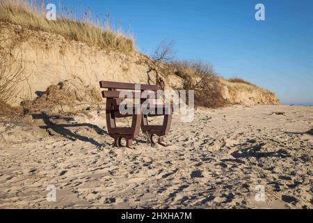 03. März 2022, Schleswig-Holstein, Nieblum: Eine freiliegende Bank steht am Strand zwischen Gotinger Cliff und FKK-Strand auf der Nordseeinsel Föhr. Die Hurrikan-Tiefstände „Nadja“ und „Zeynep“ haben zu erheblichen Schäden am Strand geführt und Düneneinbrüche auf den nordfriesischen und ostfriesischen Inseln verursacht. Nach den schweren Winterstürmen mit teilweise starken Sturmfluten rechnen viele deutsche Nordseeinseln mit erheblichen Kosten, zum Beispiel für den Wiederaufbau von abgespülten Stränden und die Erneuerung der touristischen Infrastruktur. (Zu dpa 'Inseln erwarten teilweise hohe Kosten für neue Strände nach Sturmschäden') Ph Stockfoto