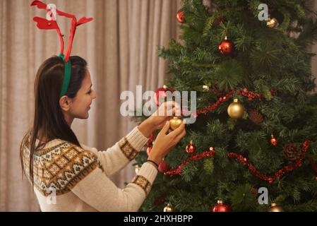 Der Weihnachtsbaum hat die letzten Feinheiten. Aufnahme einer attraktiven jungen Frau, die den Weihnachtsbaum schmückt. Stockfoto