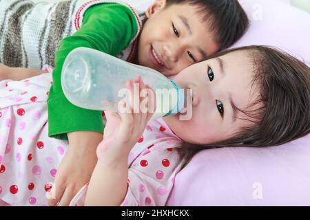 Nahaufnahme asiatische Geschwister mit glücklich im Bett vor dem Schlafen. Schwester saugt Milch auf. Bruder umarmt seine Schwester. Konzeptuelles Bild über Liebe und Bindung von s Stockfoto