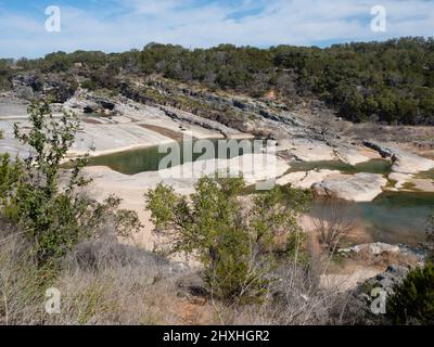 Blick auf die Pedernales Falls mit Kalksteinformationen im Pedernales Falls State Park in Texas. Zwei Wanderer stehen am oberen Pool. Stockfoto