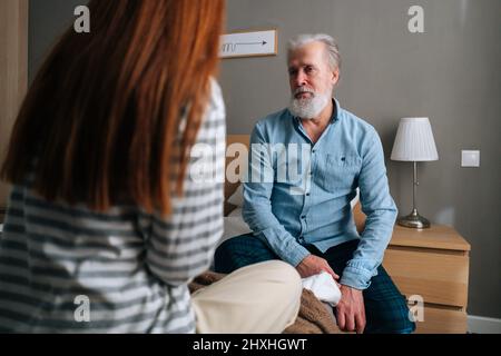 Rückansicht einer liebenden jungen Enkelin, die mit einem grauhaarigen Großvater im Bett im gemütlichen Schlafzimmer sprach. Stockfoto