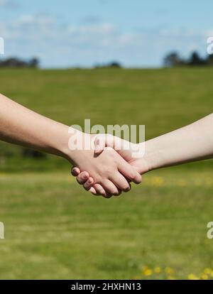 Freunde bis zum Ende. Kurzer Schuss von zwei nicht identifizierbaren Personen, die Hände halten, während sie auf einem grasbewachsenen Feld stehen. Stockfoto