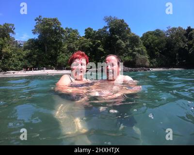 Porträt eines älteren Paares, das im Ozean schwimmt, mit tropischem Strand im Hintergrund Stockfoto