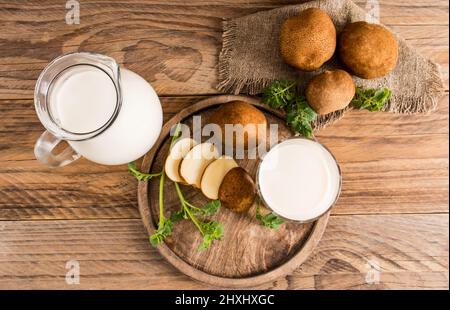 Draufsicht auf Kartoffelpflanzenmilch in einem Krug und Glas, gehackte Kartoffelscheiben, Blätter, Knollen auf einem Holztisch Stockfoto