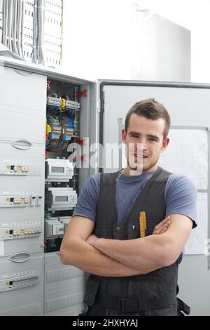 Elektroarbeiten stellen für ihn kein Problem dar. Junge Fremdfirma, die neben einer Elektroverteilertafel steht. Stockfoto