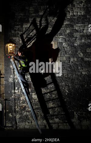 Jim, ein Feuerzeugingenieur für Gaslampen von British Gas, dreht die mechanische Uhr der ältesten Gaslampe in England, in Dean's Yard, Westminster Abbey, London, Die seit über 200 Jahren im Einsatz ist und früher eine Öllampe war. In Westminster sind noch immer über 300 Gaslampen vorhanden, und rund 1.500 Gaslampen, die 200 Jahre alt sind, leuchten weiterhin die Hauptstadt. Bilddatum: Dienstag, 8. März 2022. Stockfoto