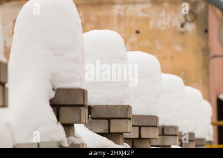 Große, schöne Säulen aus weißem Schnee auf Ziegelsteinsäulen. Eine gerade Reihe kleiner Schneeverwehungen vor dem Hintergrund einer schäbigen Wand. Urbane Winterlandschaft. Wolkiger Wintertag, weiches Licht. Stockfoto