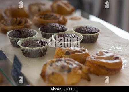Verschiedene gebackene Muffins und Brötchen in Glasvitrine im Bäckercafe. Donuts und Ringe. Im Café liegen heiße Backwaren auf dem Regal. Brötchen und Schokoladenmuffi Stockfoto
