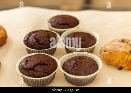 Verschiedene gebackene Muffins und Brötchen in Glasvitrine im Bäckercafe. Donuts und Ringe. Im Café liegen heiße Backwaren auf dem Regal. Brötchen und Schokoladenmuffi Stockfoto