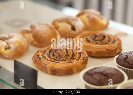 Verschiedene gebackene Muffins und Brötchen in Glasvitrine im Bäckercafe. Donuts und Ringe. Im Café liegen heiße Backwaren auf dem Regal. Brötchen und Schokoladenmuffi Stockfoto