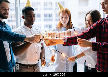 Ein glückliches Geschäftsteam aus jungen, multiethnischen Startup-Geschäftsleuten, die bei einer Firmenfeier bengalische Lichter und knallende Gläser Champagner halten Stockfoto