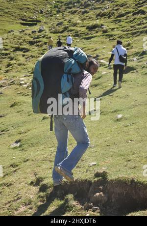 Rückansicht eines männlichen Reisenden, der mit seinen Freunden mit einem Rucksack mit Fallschirm in den Berg läuft Stockfoto