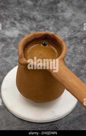 Türkischer Kaffee in einer irdenen Kanne auf dunklem Hintergrund. Geschmack der traditionellen türkischen Küche. Nahaufnahme Stockfoto