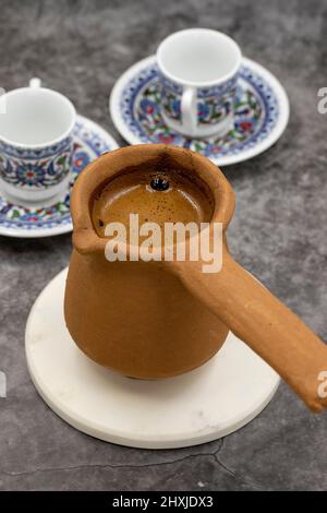 Türkischer Kaffee in einer irdenen Kanne auf dunklem Hintergrund. Geschmack der traditionellen türkischen Küche. Nahaufnahme Stockfoto