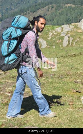 Seitenansicht eines männlichen Reisenden, der die Kamera anschaut, während er auf dem Berg mit einem Rucksack mit Fallschirm unterwegs ist Stockfoto