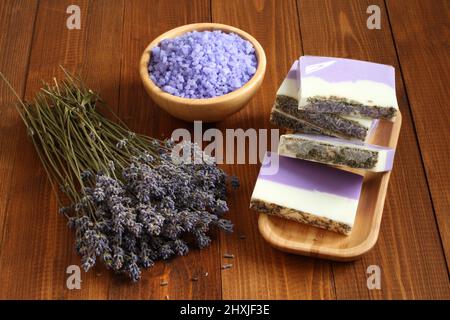 Meersalz mit Lavendel in einer Bambusschale befinden sich Seife aus Lavendel, Olivenöl und Kakaobutter auf einem Bambusteller und getrocknete Lavendelblüten Stockfoto