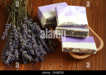 Meersalz mit Lavendel in einer Bambusschale befinden sich Seife aus Lavendel, Olivenöl und Kakaobutter auf einem Bambusteller und getrocknete Lavendelblüten Stockfoto