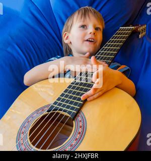 Der kleine Junge spielt Gitarre und singt auf dem Balkon Stockfoto