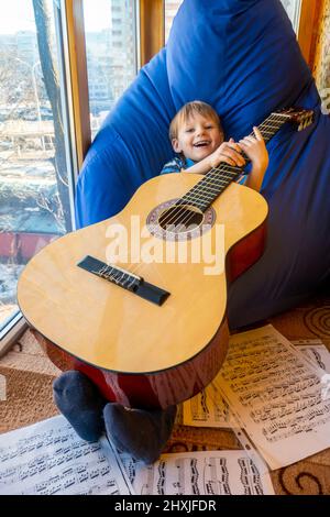 Der kleine Junge spielt Gitarre und singt auf dem Balkon Stockfoto