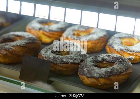 Verschiedene gebackene Puddingkuchen in Glasvitrine im Bäckercafe. Donuts und Ringe. Im Café liegen heiße Backwaren auf dem Regal. Stockfoto