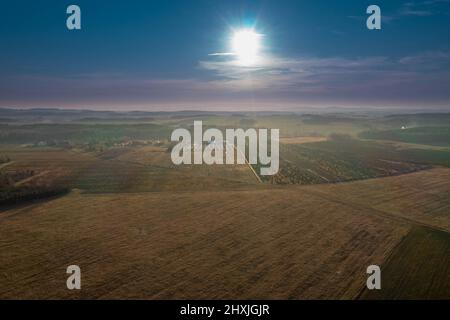 Weites, flaches Gelände, bedeckt mit Ackerfeldern und Wiesen von oben gesehen. In der Ferne sieht man die Gipfel der Berge. Stockfoto