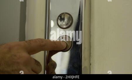 Mann Finger greift in und drückt Aufzug-Taste, die leuchtet. HDR. Nahaufnahme von Metallknöpfen eines öffentlichen Aufzugs. Stockfoto