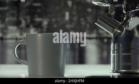 Nahaufnahme eines Gaskochers aus poliertem Stahl, der auf dem Tisch neben dem Becher steht. Aktion. Gemütliche Atmosphäre in der Küche in grauen Farben zu Hause. Stockfoto