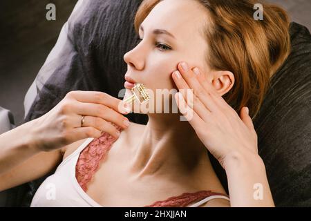 Fokussierte Frau massiert ihr Gesicht mit einem Gua Sha-Walze mit einer Spitze Stockfoto