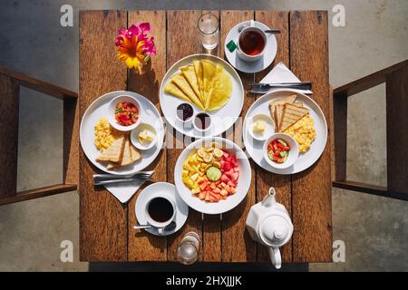 Hotelfrühstück für zwei Personen. Blick von der Tischplatte mit Rührei, Pfannkuchen, Obstsalat und Kaffee und Tee. Stockfoto