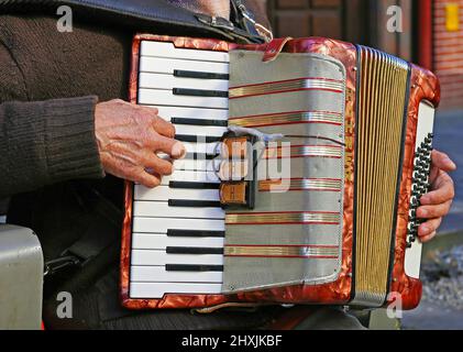 Düsseldorf, Deutschland - März 9. 2022: Nahaufnahme eines nicht erkennbaren alten Mannes, der auf einer Bank sitzt und auf einer öffentlichen Straße zweihändige hohner Student Piano Akkordeon spielt Stockfoto