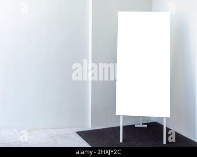 Weißer, leerer Standbanner auf weißem Wandhintergrund mit Platz zum Kopieren. Werbemockup-Zeichenfläche für Bilder oder Shop-Informationen. Standschild Stockfoto