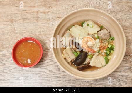 Gekochter Reis mit Meeresfrüchten und Schweineknochen in klarer Suppe auf einer Schüssel mit würziger Sauce Stockfoto