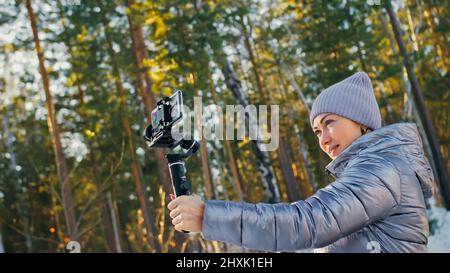 Frau, die auf einem Handheld-Film hält 3-Achsen-Gimbal-Stabilisiergerät im Winter für Smartphone. Girl Blogger Make Selfie, Broadcast Video Blogging, Vlogging. Videograf Operator Nimmt Fotovideo Auf. Stockfoto