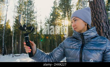 Frau, die auf einem Handheld-Film hält 3-Achsen-Gimbal-Stabilisiergerät im Winter für Smartphone. Girl Blogger Make Selfie, Broadcast Video Blogging, Vlogging. Videograf Operator Nimmt Fotovideo Auf. Stockfoto