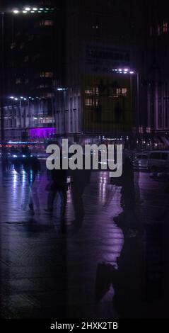 Spiegelung im Schaufenster von Silhouetten, die an einem nassen Winterabend am Strand, Liverpool entlang laufen. Stockfoto