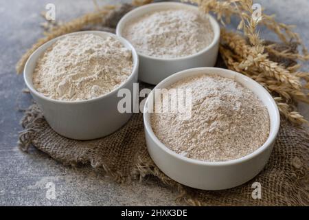 Lebensmittel und Backzutat. Weizenmehl grob aus Vollkorngetreide, Weizenkleie und Weizenmehl auf grauem Steingrund. Stockfoto