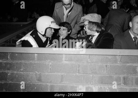 Ein Polizist im Gespräch mit Graham Taylor und Elton John, die das Fußballspiel beobachten, West Bromwich Albion gegen Watford. 25. Oktober 1977. Stockfoto